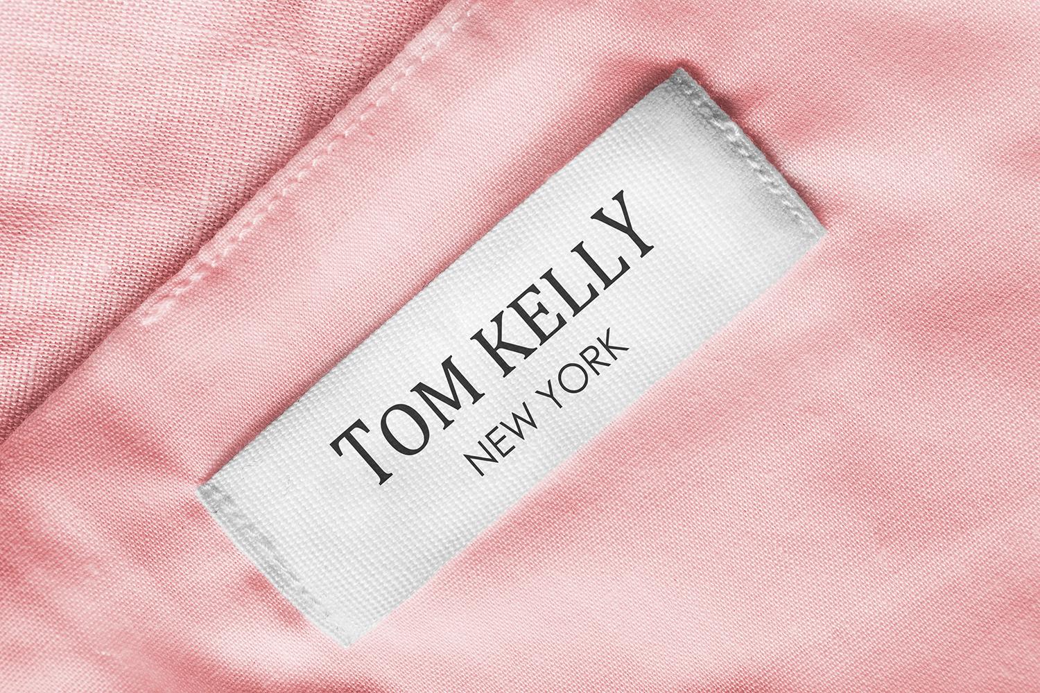 Close up of a white clothing tag sewn into pink fabric that reads TOM KELLY NEW YORK